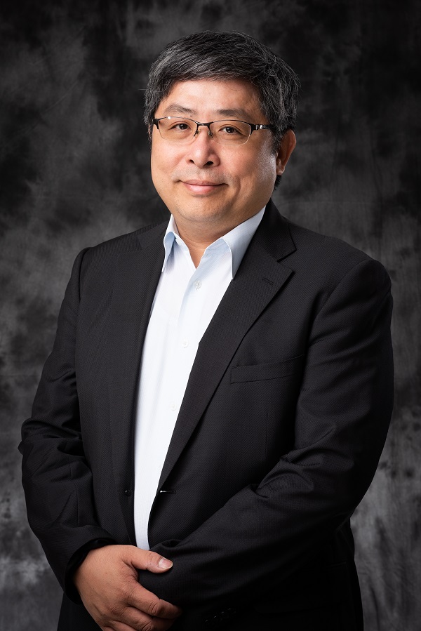 Portrait of Wen-hua Kuo in a black suit jacket and white tie, with black and grey heair and wire glasses. The background is a black cloudy studio background.