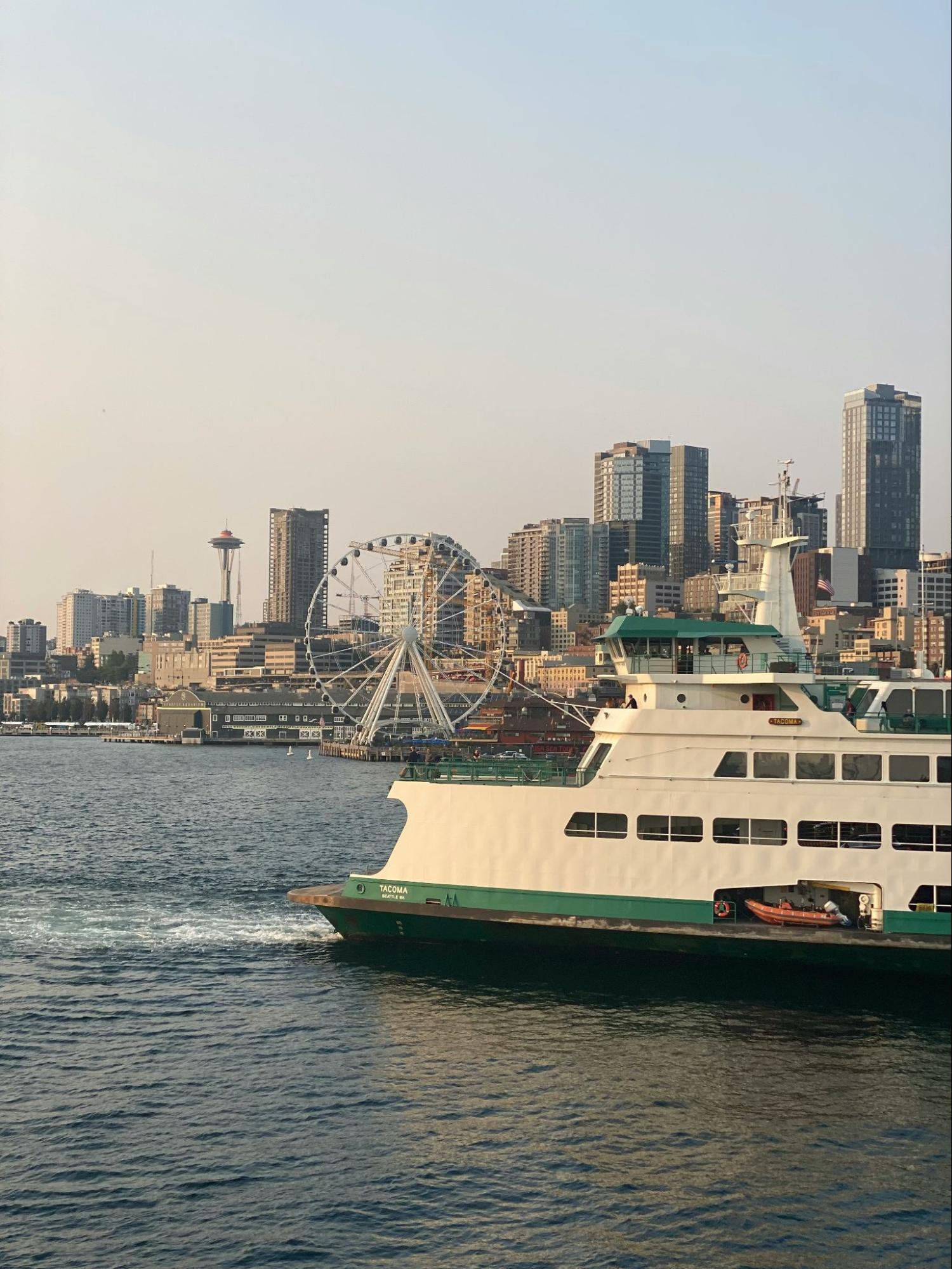 Photograph of a Washington State Ferry with the Seattle skyline in the background, featuring the Seattle Great Wheel and the Space Needle